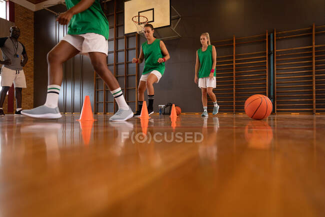 Diverso equipo femenino de baloncesto y entrenador practican driblando pelota. baloncesto, entrenamiento deportivo en una cancha cubierta. - foto de stock