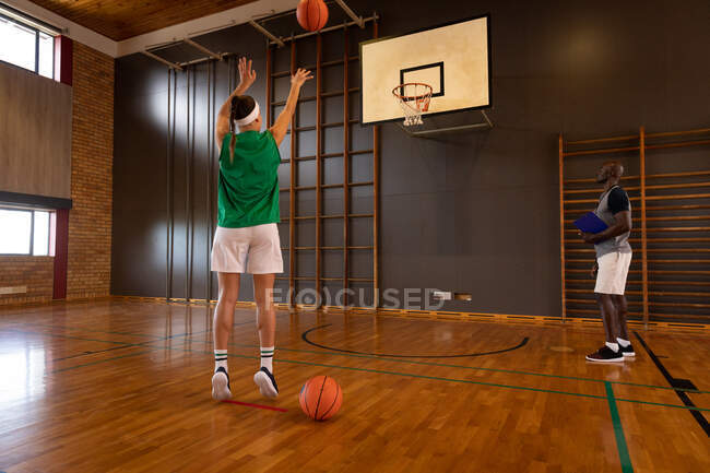 Кавказская баскетболистка и тренер по стрельбе мячом. баскетбол, спортивные тренировки на крытой площадке. — стоковое фото