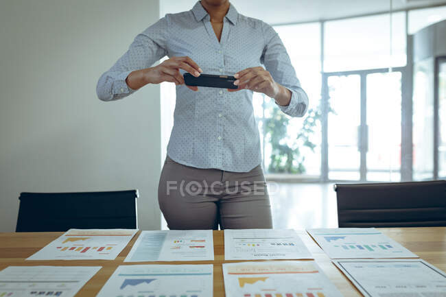Gemischte Geschäftsfrau fotografiert Dokumente auf dem Schreibtisch mit dem Smartphone. Arbeit in einem unabhängigen kreativen Unternehmen. — Stockfoto