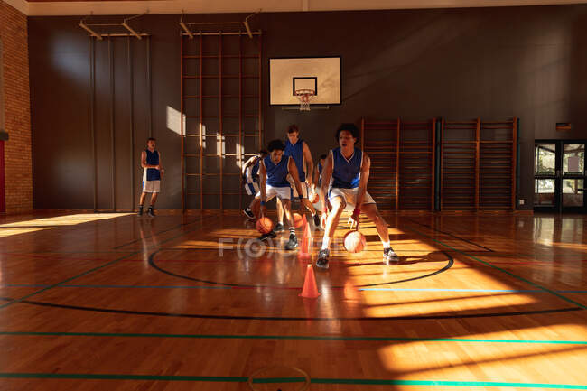 Une équipe masculine diversifiée de basket portant des vêtements de sport bleus et pratiquant le dribble ball. basket-ball, entraînement sportif sur un terrain intérieur. — Photo de stock