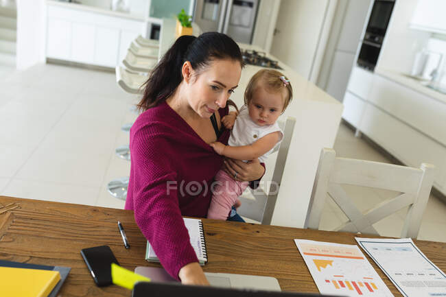 Mãe branca segurando seu bebê usando laptop enquanto trabalhava em casa. maternidade, amor e conceito de cuidado do bebê — Fotografia de Stock