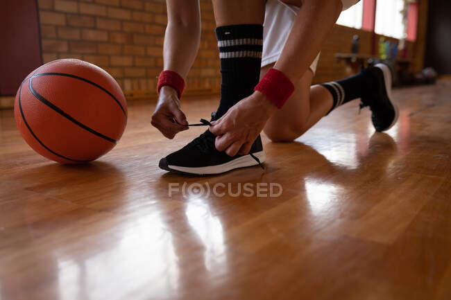 Jogador de basquete feminino amarrando sapatos e vestindo roupas esportivas. basquete, treinamento esportivo em uma quadra interna. — Fotografia de Stock