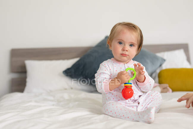 Portrait of caucasian baby playing with a toy while sitting on the bed at home. motherhood, love and baby care concept — Stock Photo