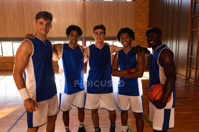 Retrato da equipe de basquete masculino diversificada sorrindo e abraçando. basquete, treinamento esportivo em uma quadra interna. — Fotografia de Stock