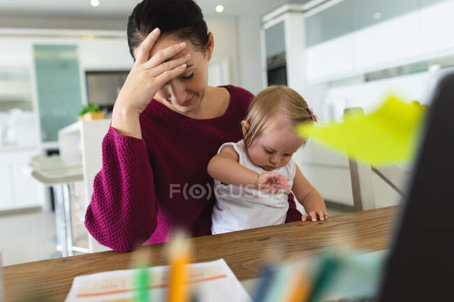 Stressed caucasian mother with her baby holding her head at home. motherhood, love and baby care concept — Stock Photo