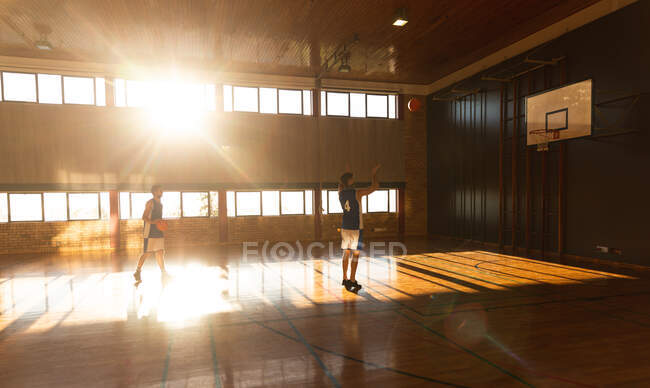 Deux joueurs masculins différents pratiquant le tir au ballon. basket-ball, entraînement sportif sur un terrain intérieur. — Photo de stock
