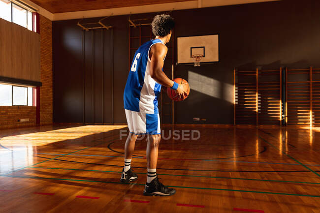 Jugador de baloncesto masculino de raza mixta practicando tiro con pelota. baloncesto, entrenamiento deportivo en una cancha cubierta. - foto de stock