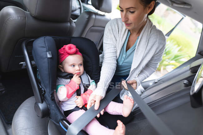 Madre caucásica poniendo a su bebé en asiento de seguridad en el coche. maternidad, amor y cuidado del bebé - foto de stock