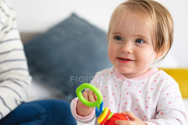 Bebê caucasiano sorrindo enquanto brincava com um brinquedo sentado na cama em casa. maternidade, amor e conceito de cuidado do bebê — Fotografia de Stock