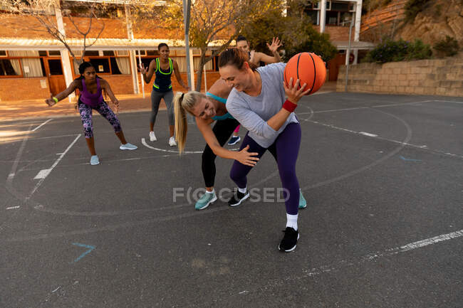 Equipo de baloncesto femenino diverso que usa ropa deportiva y practica driblar pelota. baloncesto, entrenamiento deportivo en una cancha urbana al aire libre. - foto de stock
