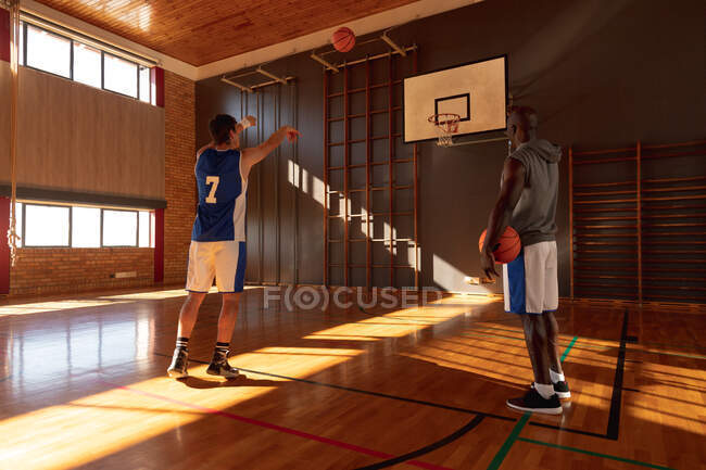 Caucásico jugador de baloncesto masculino y entrenador practicando tiro con pelota. baloncesto, entrenamiento deportivo en una cancha cubierta. - foto de stock