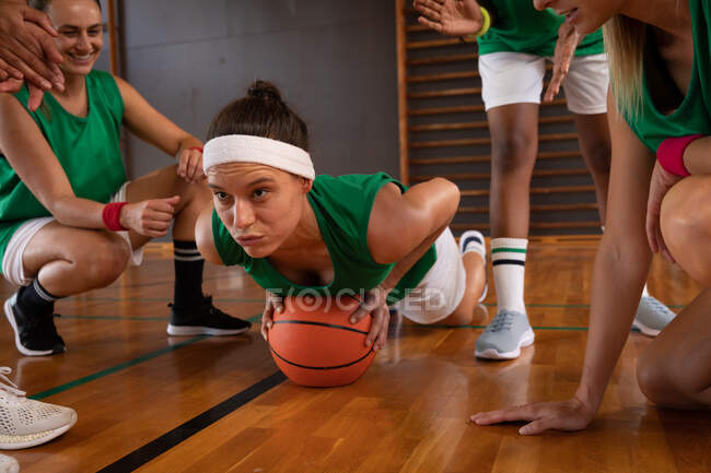 Equipo de baloncesto femenino diverso usando ropa deportiva y haciendo flexiones. baloncesto, entrenamiento deportivo en una cancha cubierta. - foto de stock