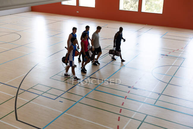 Equipe masculine diversifiée de basket-ball et entraîneur quittant la salle de gym après match. basket-ball, entraînement sportif sur un terrain intérieur. — Photo de stock