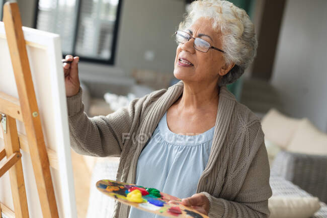 Gemischte Rennen Seniorin Malerei auf Leinwand im Wohnzimmer. Isolationshaft während der Quarantäne. — Stockfoto