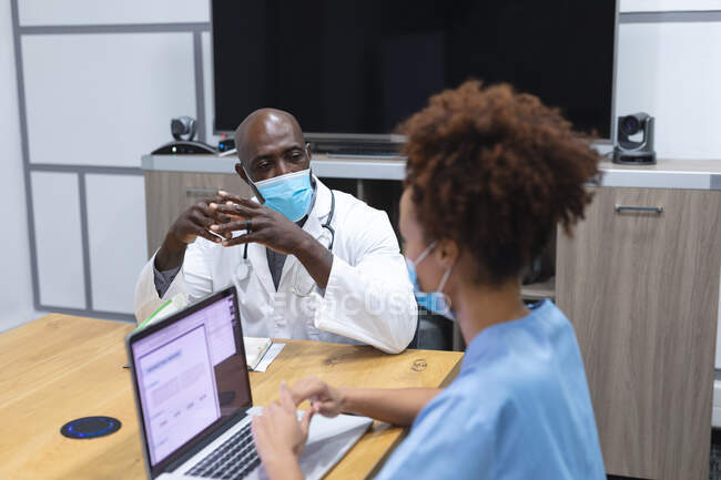 Diverse male doctor and female nurse wearing face masks, using laptop and talking. medicine, health and healthcare services during coronavirus covid 19 pandemic. — Stock Photo