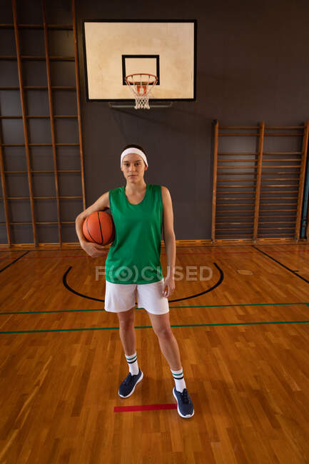 Портрет белой баскетболистки, держащей мяч. баскетбол, спортивные тренировки на крытой площадке. — стоковое фото