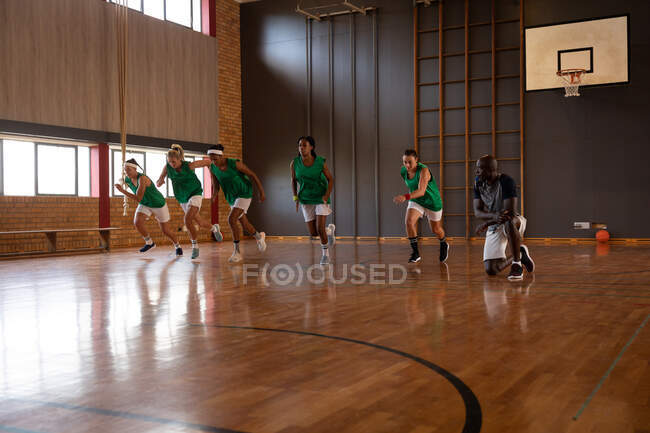 Разнообразная женская баскетбольная команда и тренер в спортивной одежде и беге. баскетбол, спортивные тренировки на крытой площадке. — стоковое фото