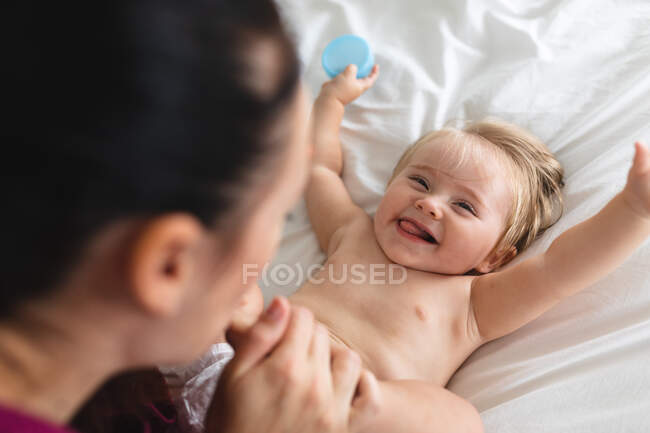 Madre caucásica besando los pies de su bebé mientras está sentada en la cama en casa. maternidad, amor y cuidado del bebé - foto de stock
