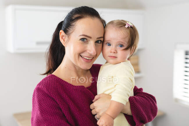 Portrait of caucasian mother smiling while holding her baby at home. motherhood, love and baby care concept — Stock Photo