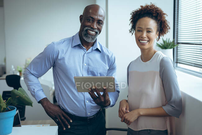 Портрет двух разнообразных коллег по бизнесу мужчин и женщин, улыбающихся и пользующихся планшетом. работа в независимом креативном бизнесе. — стоковое фото
