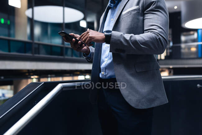 Средняя секция бизнесмена, использующего смартфон, стоящий у лестницы в офисе. бизнес и офисная концепция — стоковое фото