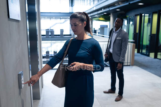 Kaukasische Geschäftsfrau mit Smartphone, die im modernen Büro den Liftknopf drückt. Geschäfts- und Bürokonzept — Stockfoto