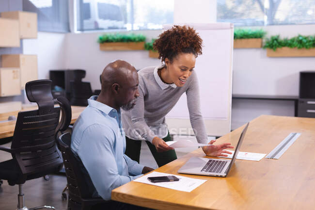 Two diverse male and female business colleagues sitting at desk, using laptop and discussing. work at an independent creative business. — Stock Photo