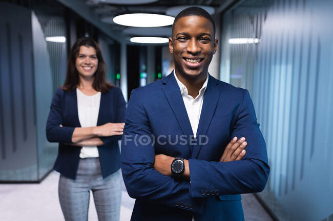 Retrato de empresário diversificado e mulher de negócios com braços cruzados sorrindo no escritório moderno. conceito de negócio e escritório — Fotografia de Stock
