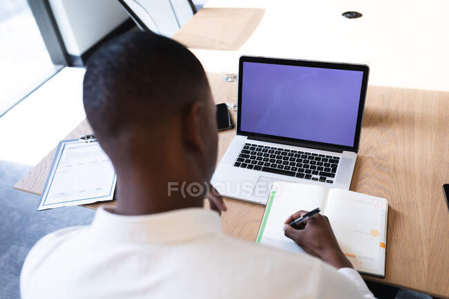 Homme d'affaires afro-américain avec ordinateur portable prenant des notes tout en étant assis dans la salle de réunion au bureau moderne. concept d'entreprise et de bureau — Photo de stock