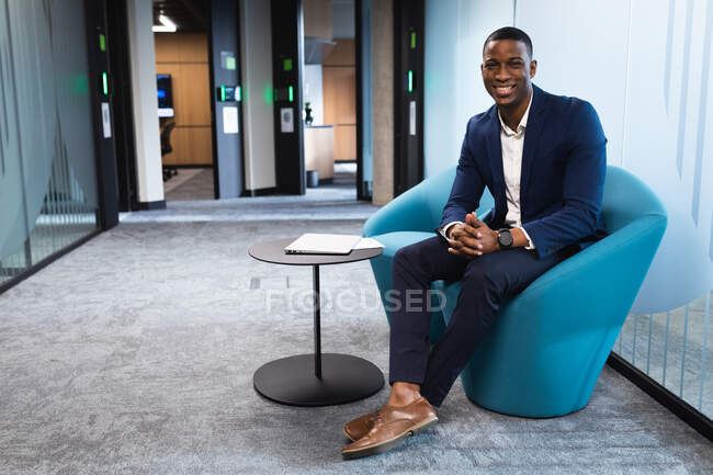 Retrato del hombre de negocios afroamericano sonriendo sentado en una silla en la oficina moderna. concepto de negocio y oficina - foto de stock