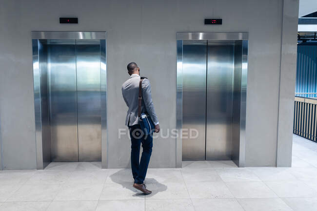 Rückansicht eines afrikanisch-amerikanischen Geschäftsmannes, der in einem modernen Büro auf den Aufzug wartet. Geschäfts- und Bürokonzept — Stockfoto