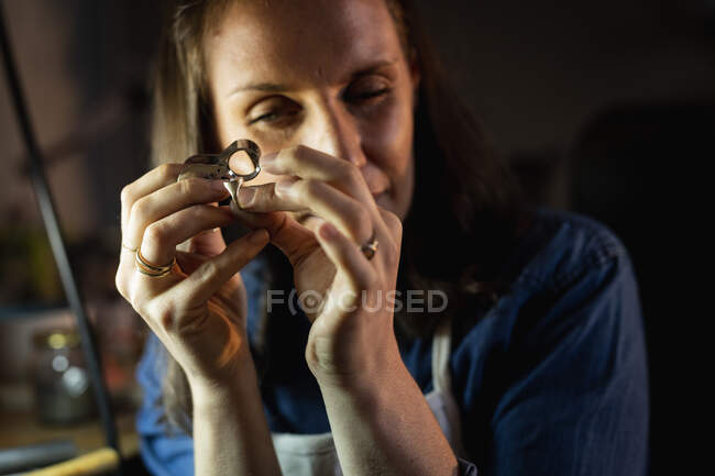 Porträt einer kaukasischen Juwelierin, die eine Schürze trägt und in der Werkstatt Schmuck herstellt. Selbstständiger Handwerksbetrieb. — Stockfoto