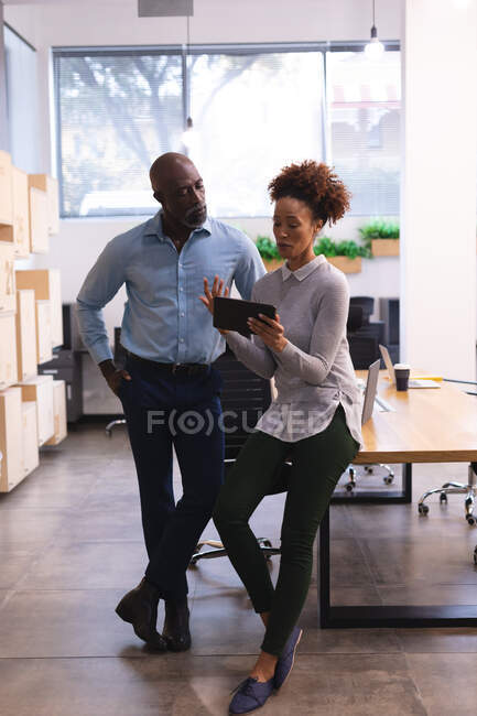 Two diverse male and female business colleagues using tablet and talking. work at an independent creative business. — Stock Photo