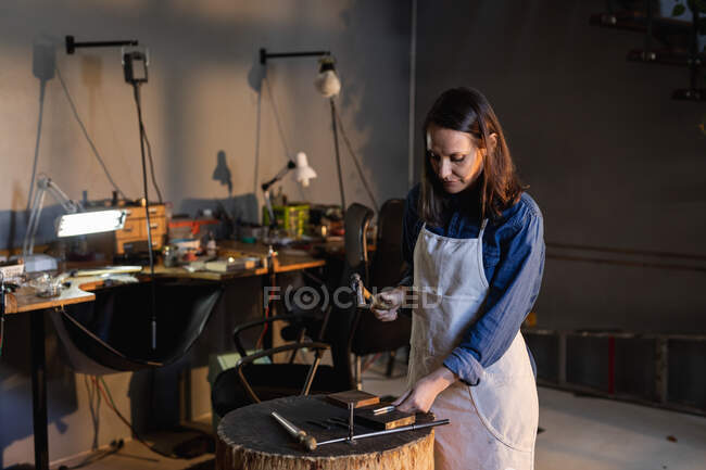 Focused caucasian female jeweller holding jewelry tools, making jewelry in workshop. independent handmade craft business. — Stock Photo