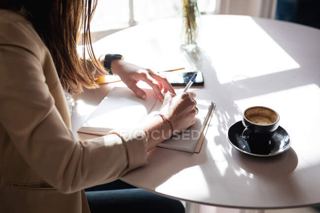 Sezione centrale della cliente caucasica seduta a tavola con il caffè, che prende appunti. piccola impresa indipendente caffè. — Foto stock
