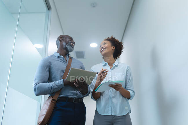 Two diverse male and female business colleagues smiling and using tablet. work at an independent creative business. — Stock Photo