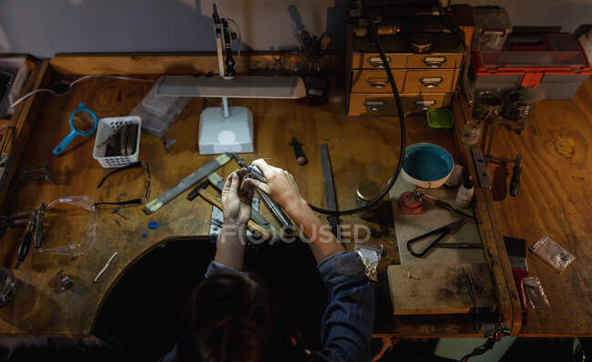 Bijouterie blanche assise au bureau, tenant des outils de bijoux, fabriquant des bijoux en atelier. entreprise artisanale indépendante. — Photo de stock