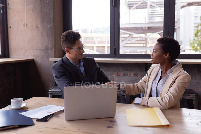 Hombre de negocios caucásico y mujer de negocios afroamericana estrechando la mano mientras se sienta en un café. concepto de empresa y asociación - foto de stock