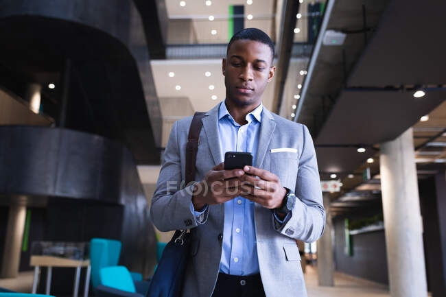 Homme d'affaires afro-américain utilisant un smartphone tout en étant debout au bureau moderne. concept d'entreprise et de bureau — Photo de stock