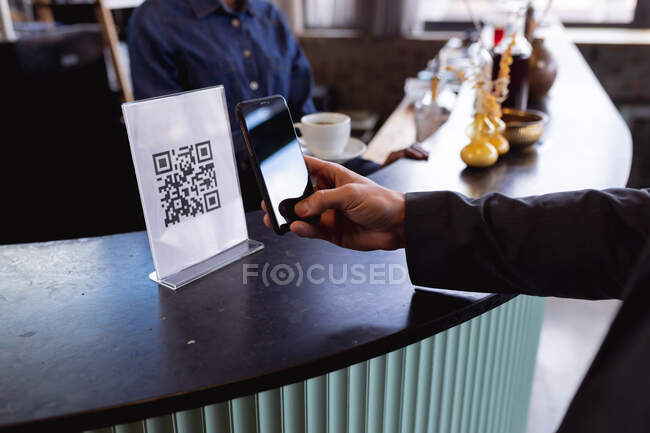 Mid section of man making a payment by scanning qr code from smartphone at a cafe. digital and cashless payment technology concept — Stock Photo