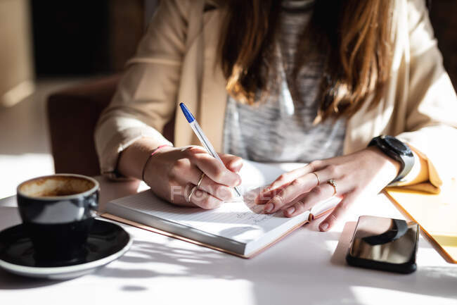 Close up of hands of female customer sitting at table, making notes. small independent cafe business. — Stock Photo