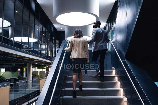 Vista trasera de diversos hombres de negocios y mujeres de negocios que suben las escaleras en la oficina moderna. concepto de negocio y oficina - foto de stock