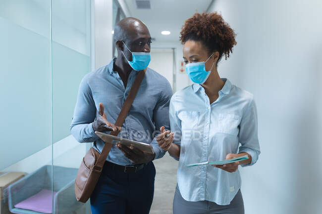 Різні чоловічі та жіночі бізнес-колеги носять маски для обличчя, використовуючи планшет та розмовляючи. робота в сучасному офісі під час пандемії коронавірусу 19 . — стокове фото