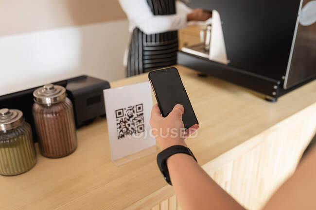 Hand of female customer standing at counter top, holding smartphone, scanning qr code. small independent cafe business. — Stock Photo