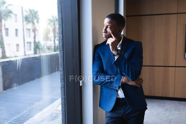 Nachdenklicher afrikanisch-amerikanischer Geschäftsmann, der aus dem Fenster auf ein modernes Büro blickt. Geschäfts- und Bürokonzept — Stockfoto