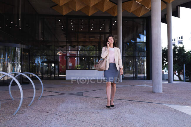 Caucasian businesswoman talking on a smartphone while walking at corporate park. business and office concept — Stock Photo