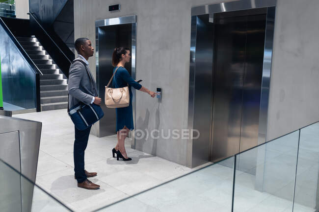 Mulher de negócios caucasiana segurando smartphone pressionando o botão de elevação no escritório moderno. conceito de negócio e escritório — Fotografia de Stock