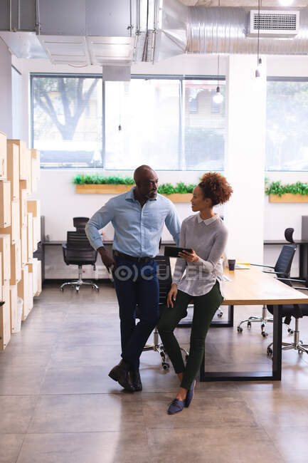 Two diverse male and female business colleagues using tablet and talking. work at an independent creative business. — Stock Photo