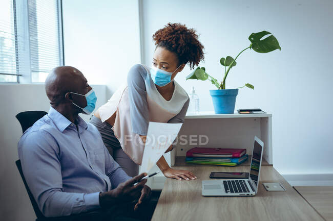 Два різних бізнес-колеги носять маски для обличчя та обговорюють. робота в сучасному офісі під час пандемії коронавірусу 19 . — стокове фото