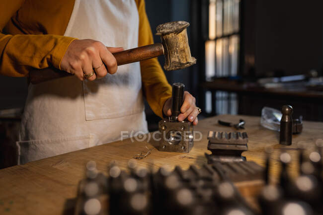 Midsection of female jeweller wearing apron, using hammer, making jewelry. independent handmade craft business. — Stock Photo